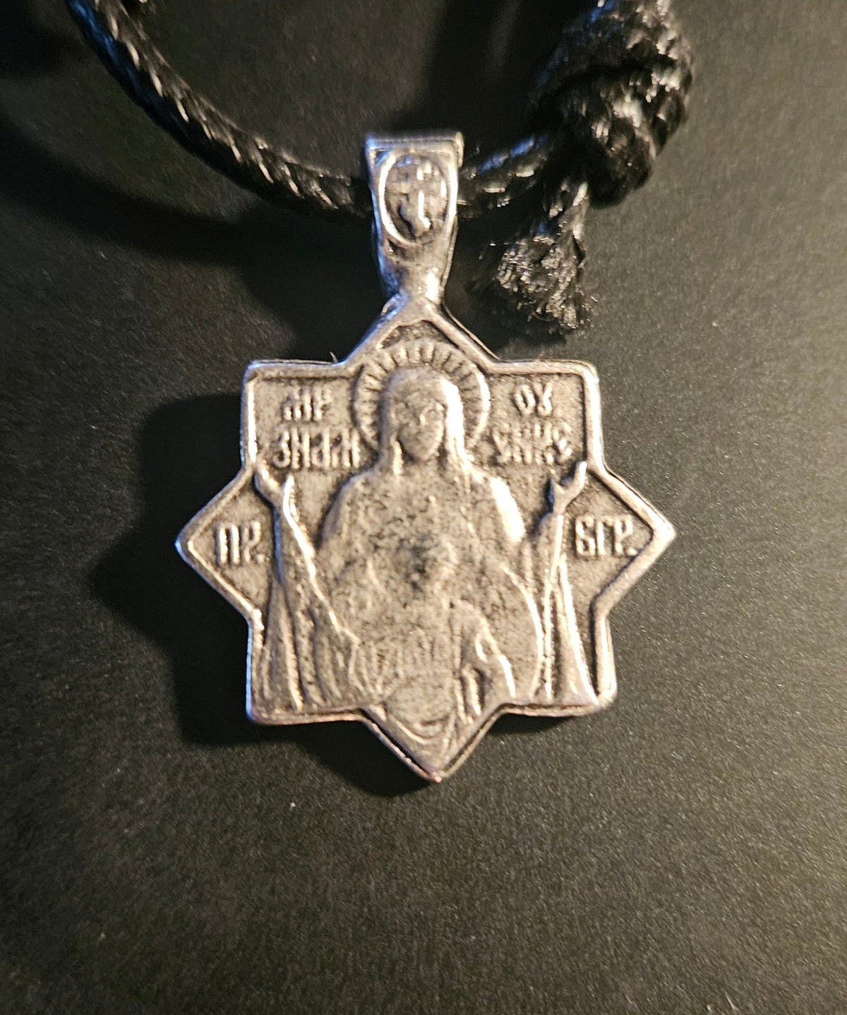 Silver pendant on a black cord against a dark background
